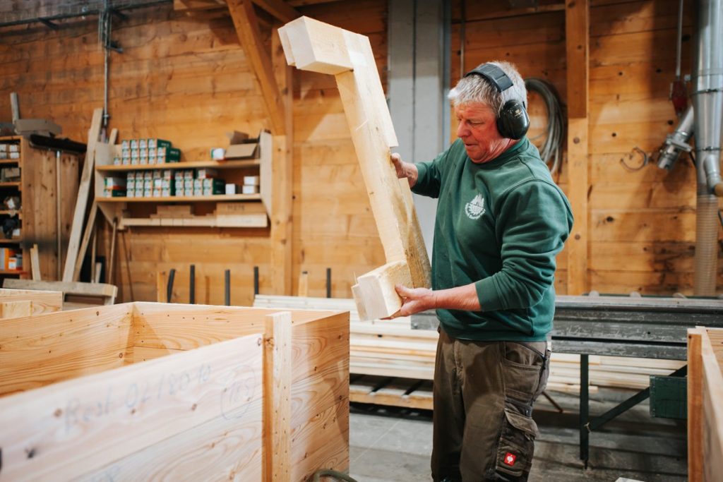 Mitarbeiter mit Gehörschutz trägt ein Holzbrett in der Werkshalle