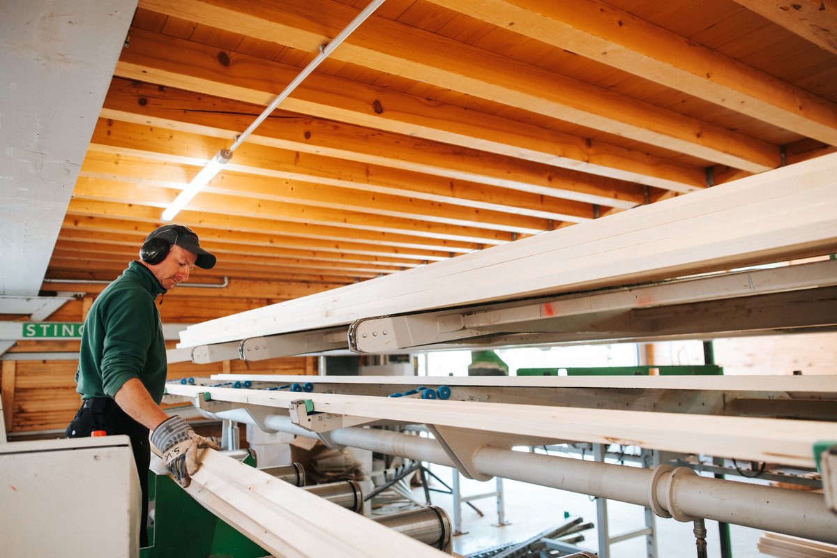 Mitarbeiter kontrolliert Holzbalken auf der Produktionslinie in der Werkshalle
