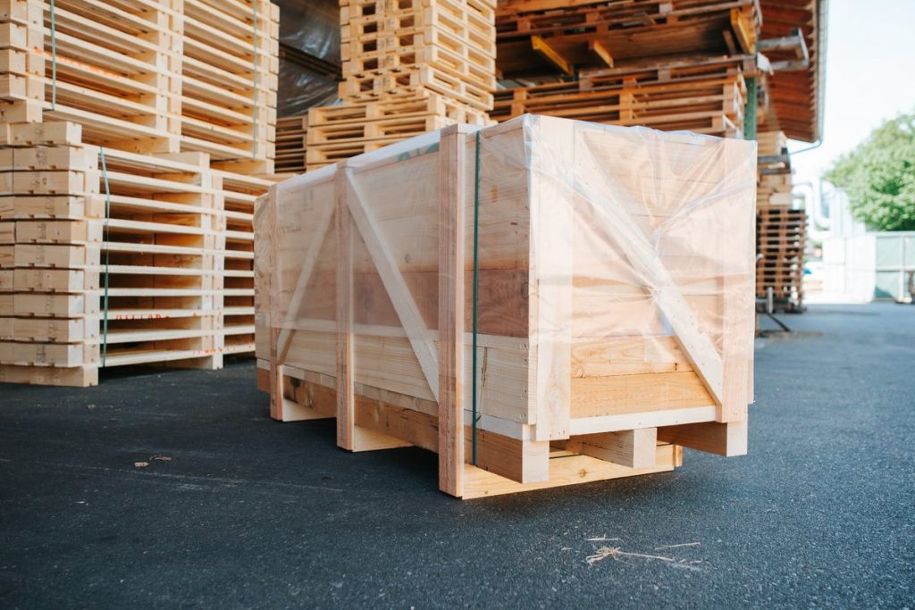 Mit Folie umwickelte Holzverpackungskiste vor gestapelten Paletten