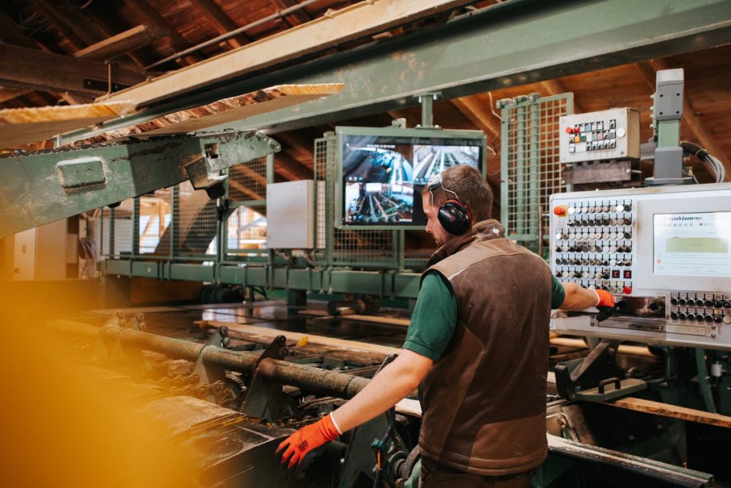 Mitarbeiter bedient eine Sägewerksmaschine mit Schutzhandschuhen