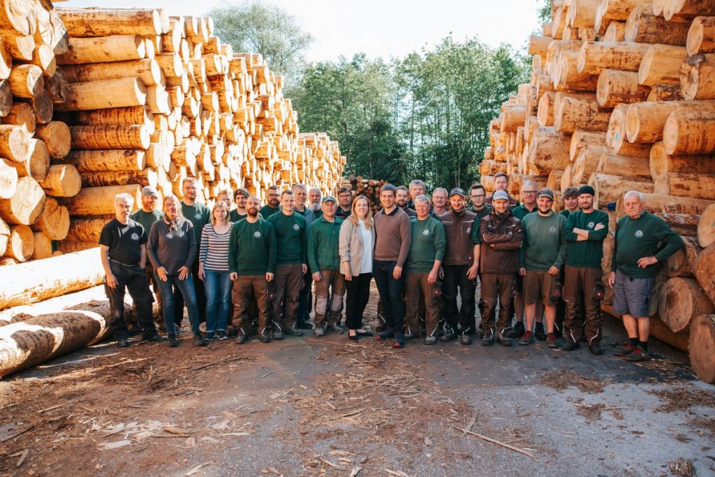 Belegschaft von Holzwerk Baumgartner bei einem Gruppenfoto vor Rundholzstapeln im Freien